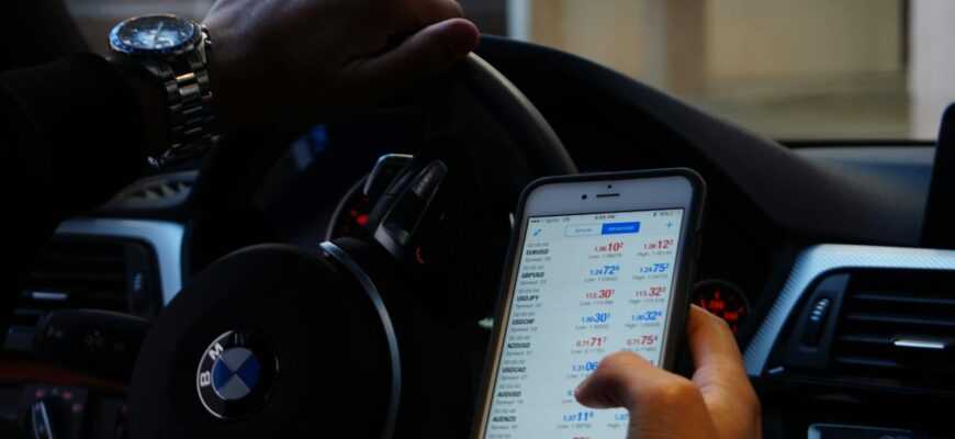 Person using mobile phone for currency trading while driving BMW car.