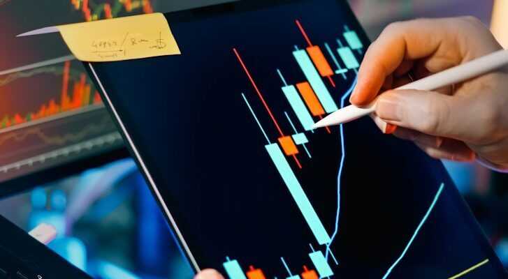 Trader analyzing stock market charts on tablet and monitor